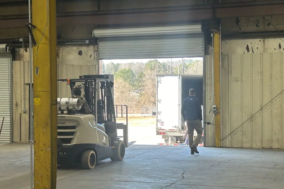 Forklift at an open warehouse dock door with a trailer backed up outside