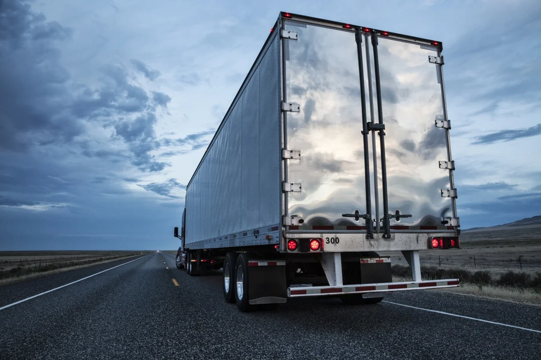 Dry van trailer pulled by a Class 8 truck down an open highway under a cloudy sky